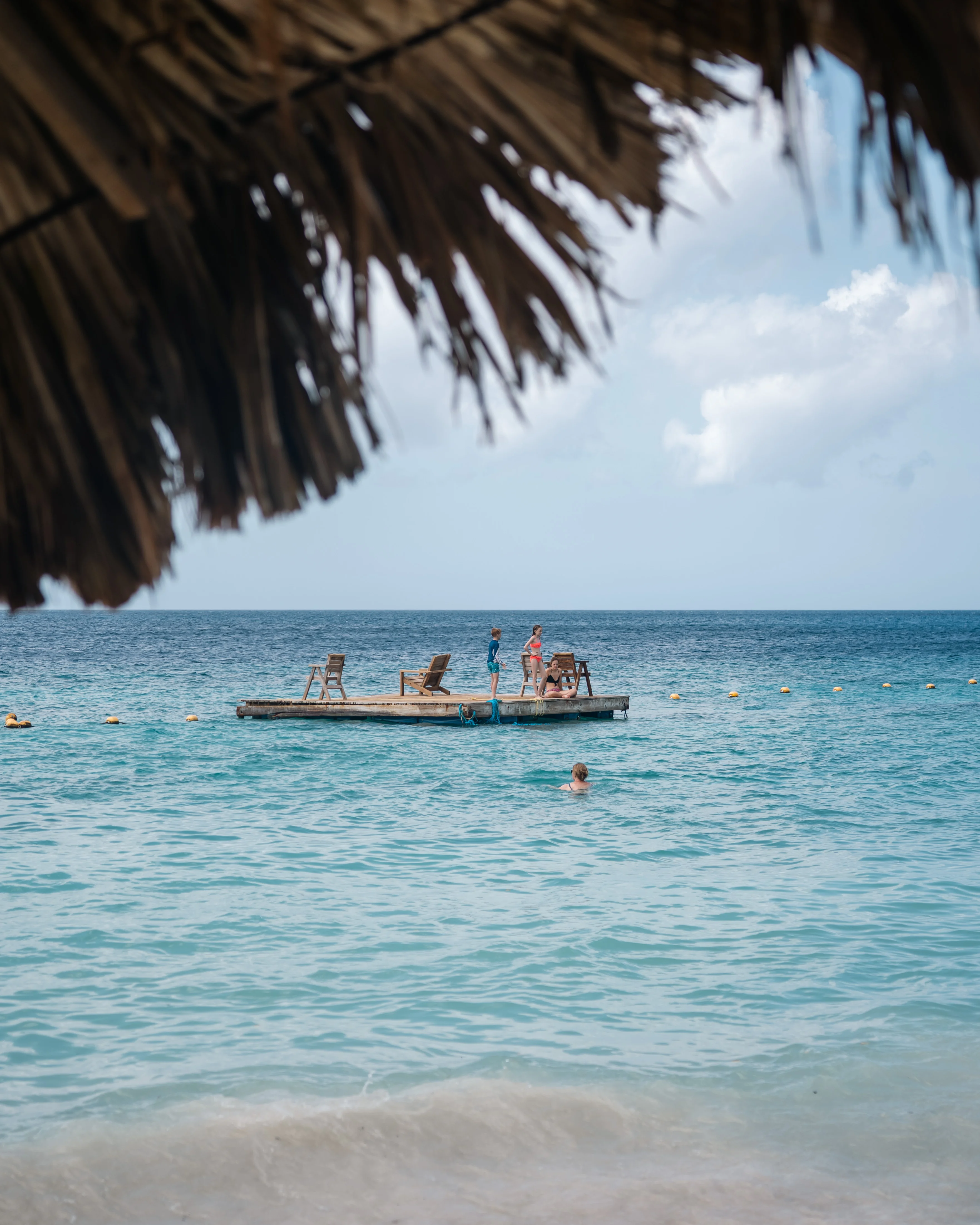 Swim platform in calm turquoise water framed by a thatched palapa roof