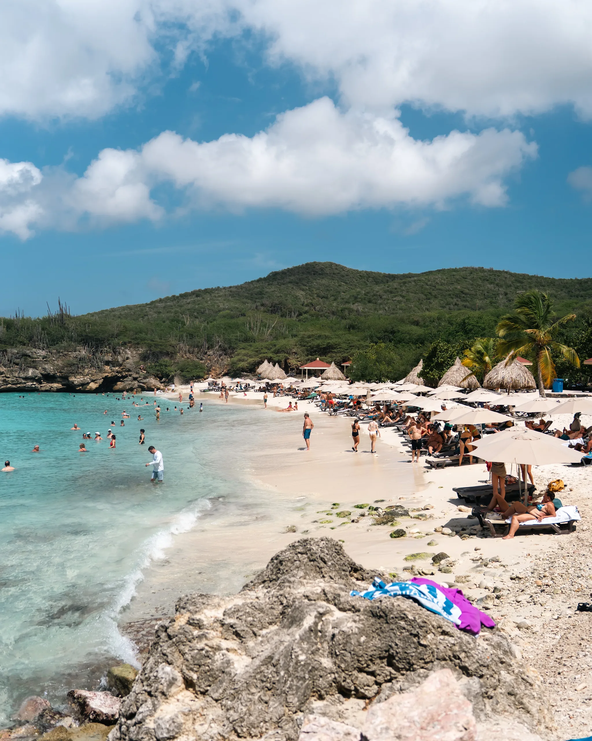 Busy white-sand cove at Kenepa with palapas and green hills behind