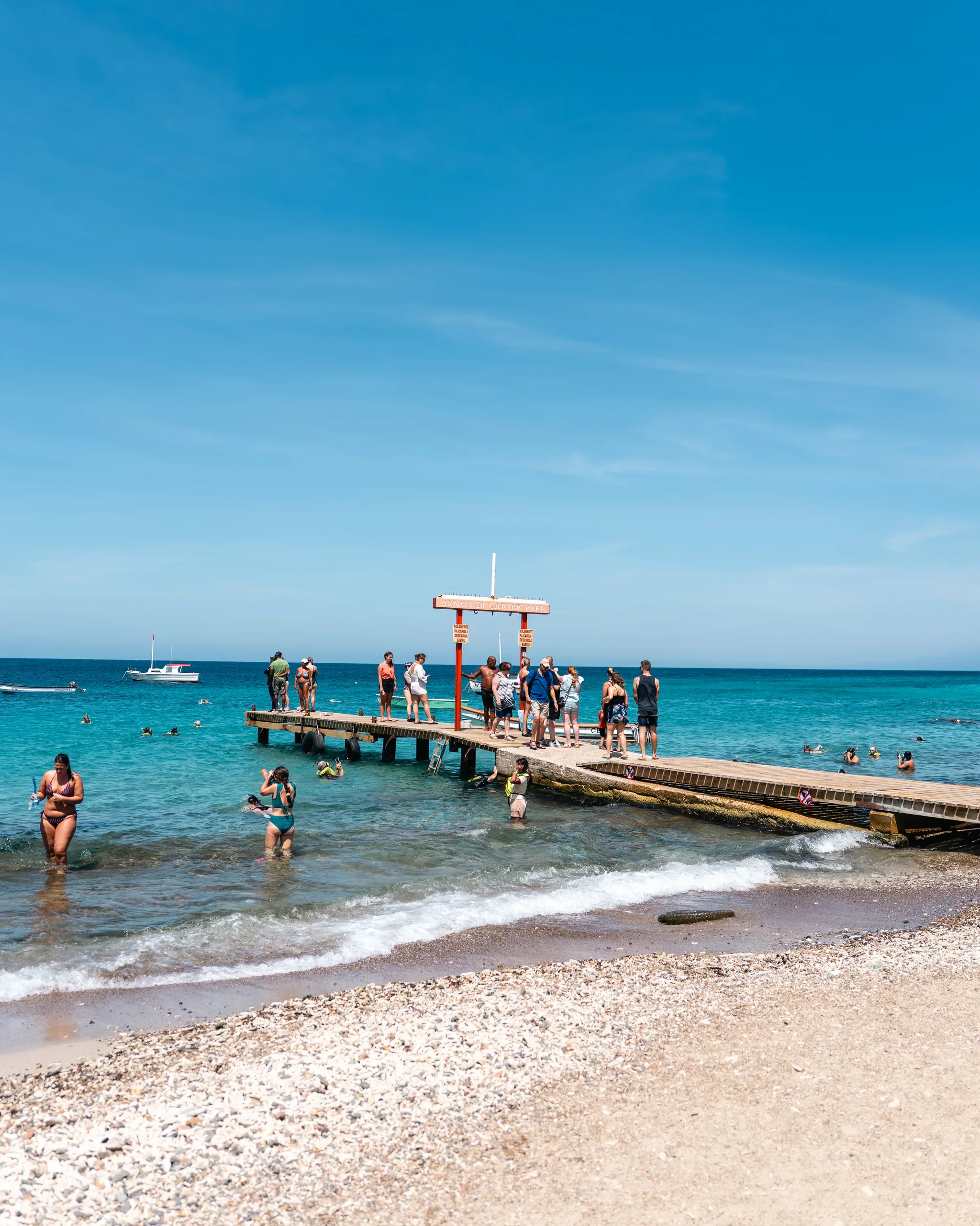 De pier van Playa Grandi gezien vanaf het strand, met hier en daar snorkelaars op het vlakke water
