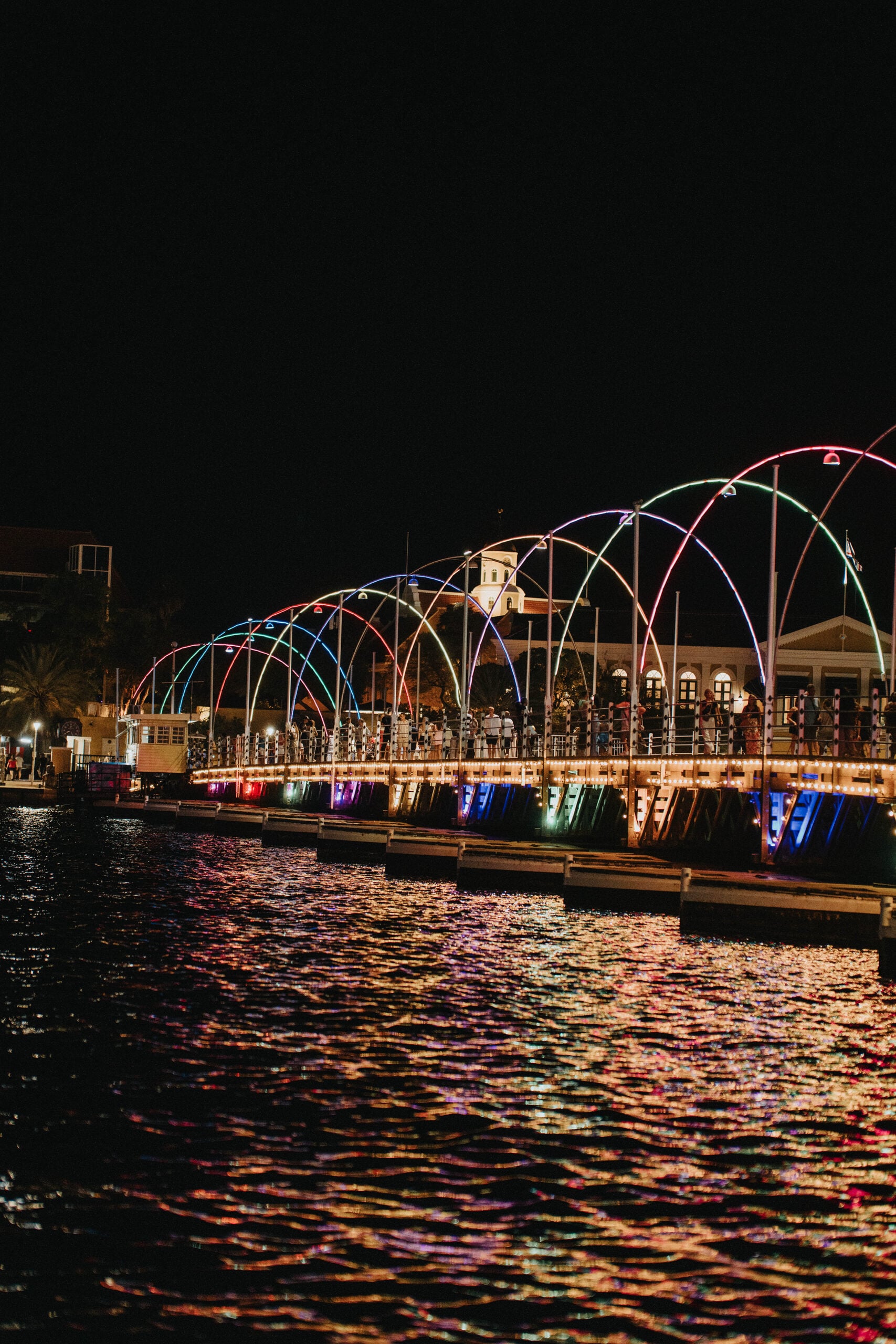 The Queen Emma pontoon bridge lit up at night, reflecting across the harbor