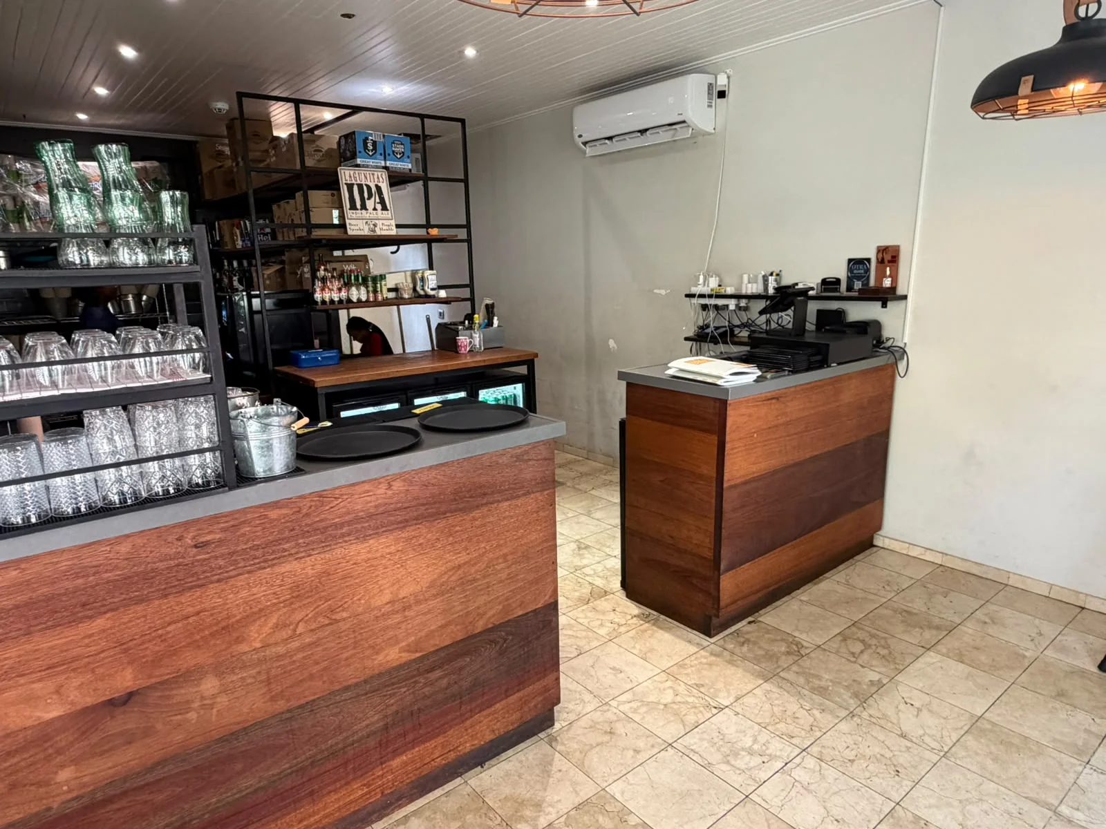 Wood-panelled bar counter inside BRGR Haus with stacked glassware, serving trays and craft beer signage.