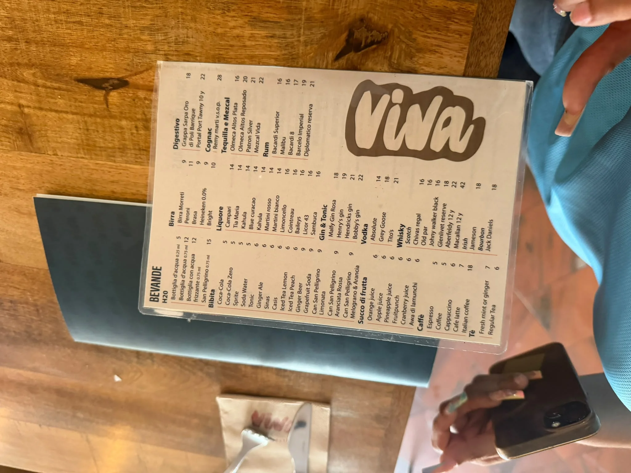 Laminierte Getränkekarte von „Bevande“ im „Viva“, auf der Wasser, Erfrischungsgetränke, Säfte, Kaffee, Bier, Liköre und Spirituosen mit Preisangaben aufgeführt sind.