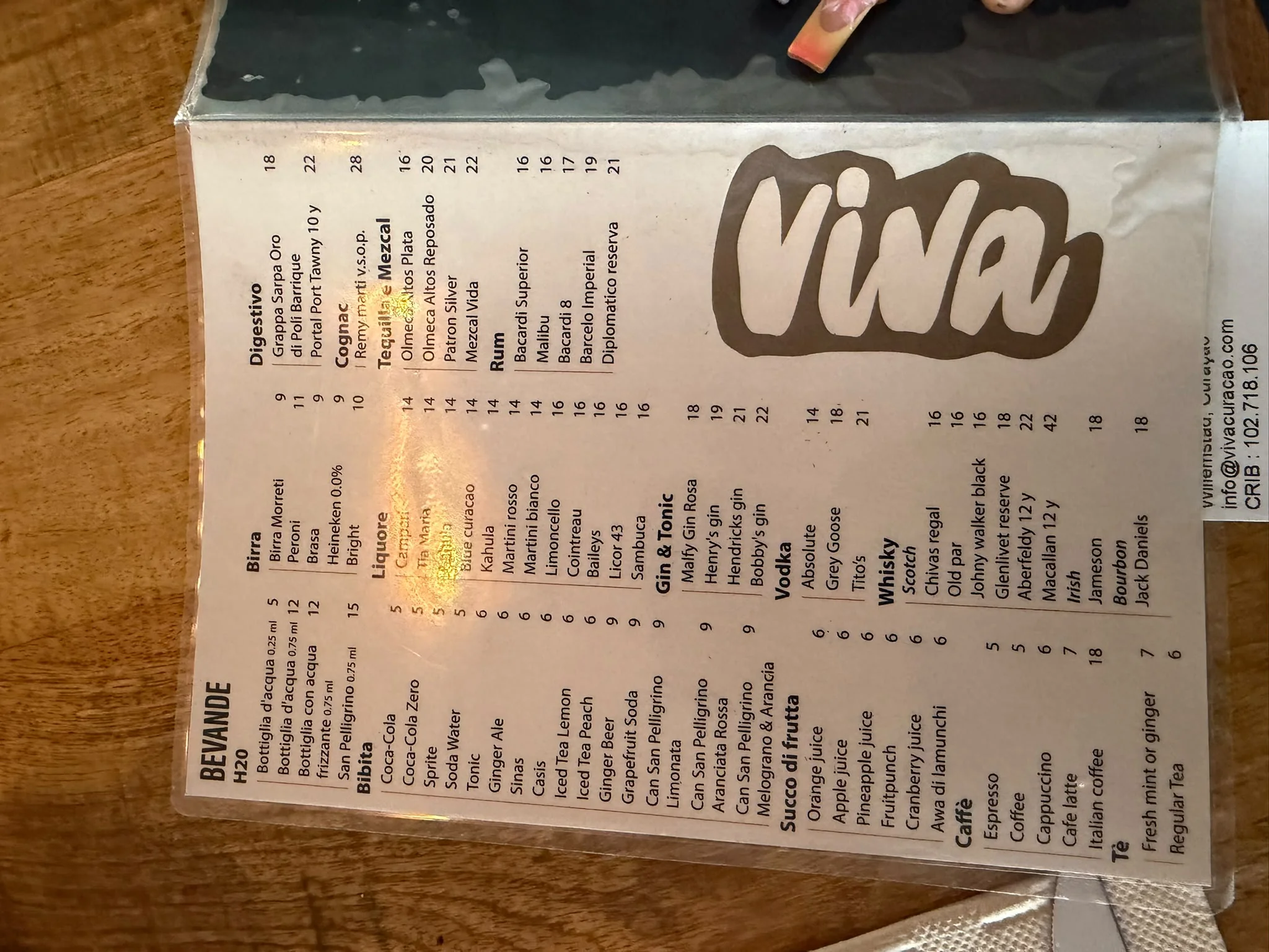 Eine Getränkekarte mit den Preisen für Whisky, Rum, Tequila und Digestifs, wobei die Kontaktdaten von „Viva“ in Willemstad auf einer Karte vermerkt sind, die in die Hülle gesteckt ist.